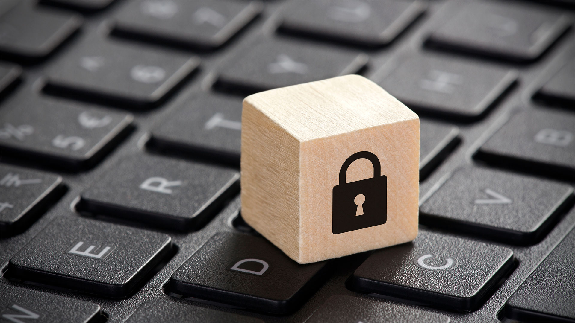 Un cubo di legno con l'icona di un lucchetto chiuso posizionato su una tastiera di computer, simboleggiando la sicurezza digitale e la tutela della privacy.